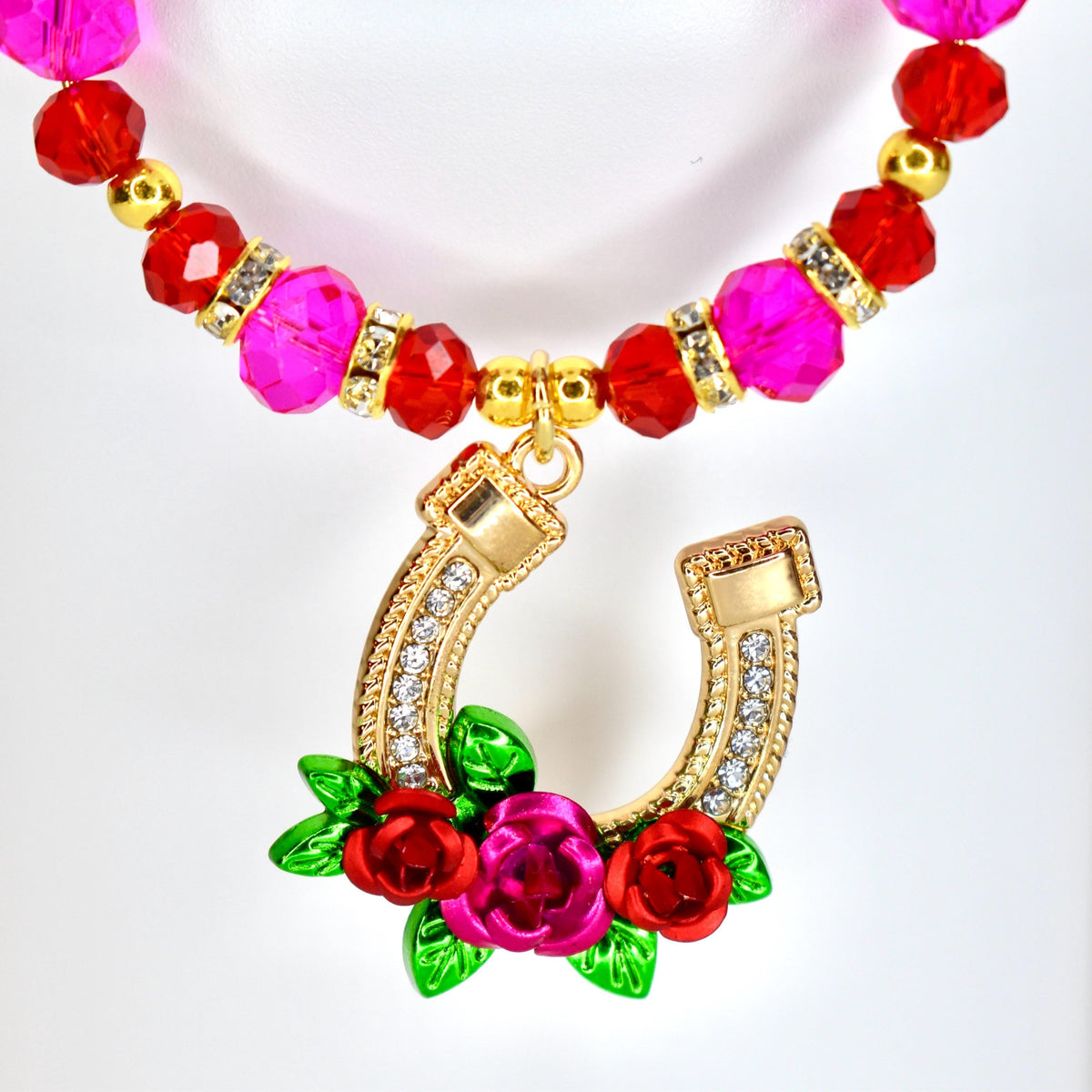 A tumbler handle charm featuring a gold-colored horseshoe pendant adorned with clear crystals and a cluster of red and pink roses with green leaves. The charm has a beaded strand of pink and red beads.