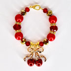 A red beaded tumbler handle charm with gold accents and a gold cherry charm. The tumbler bracelet features large red beads, faceted red beads, and gold-colored faceted beads. The charm is a pair of red cherries with a gold bow.