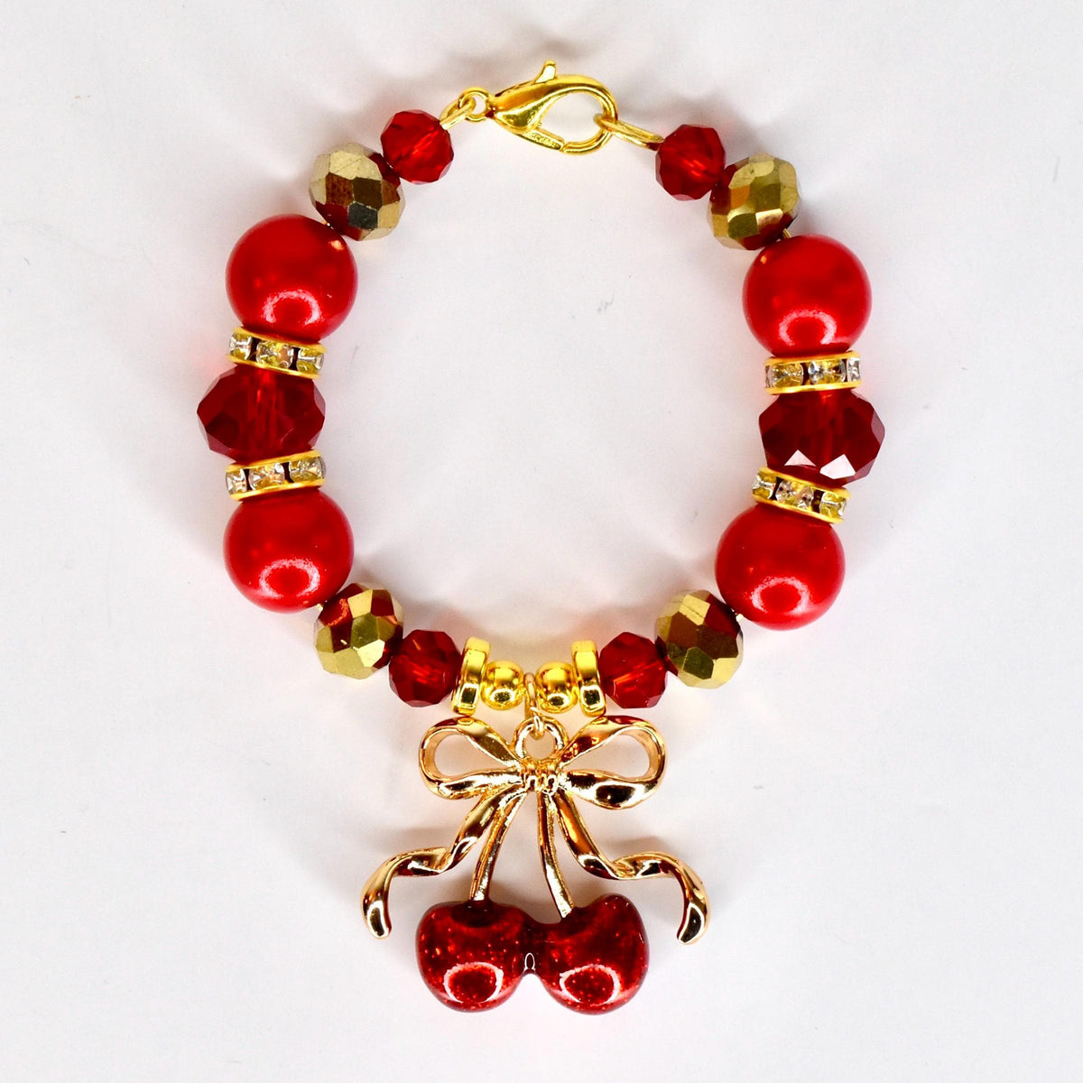 A red beaded tumbler handle charm with gold accents and a gold cherry charm. The tumbler bracelet features large red beads, faceted red beads, and gold-colored faceted beads. The charm is a pair of red cherries with a gold bow.