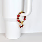 A red beaded tumbler handle bracelet with gold accents and a gold cherry charm. The bracelet features large red beads, smaller gold beads, and a gold bow with two red cherry pendants. The bracelet is displayed on a white background.