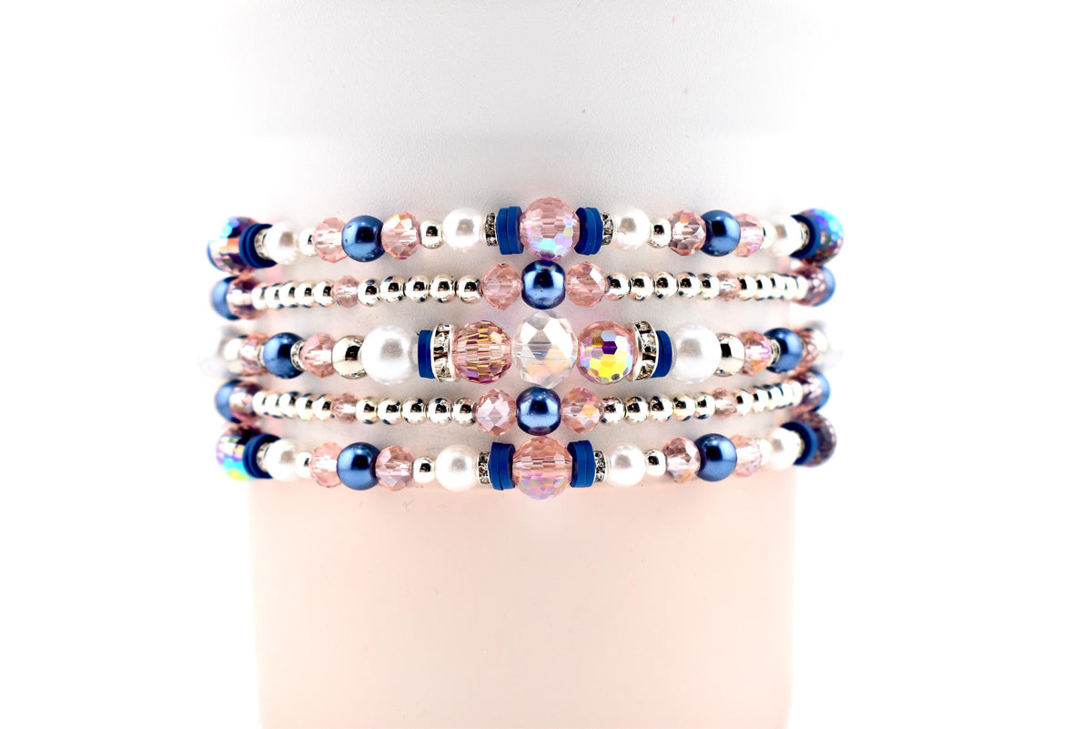 Stack of beaded bracelets with pink, white, silver, and blue beads. The bracelets feature a mix of pearl, crystal, and metallic beads. The bracelets are stacked on top of each other.