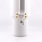 A graduation-themed bracelet with white faux pearls, gold beads, and clear crystals. A small silver graduation cap charm and key charm dangle from the bracelet. The bracelet is displayed on a white mug handle.