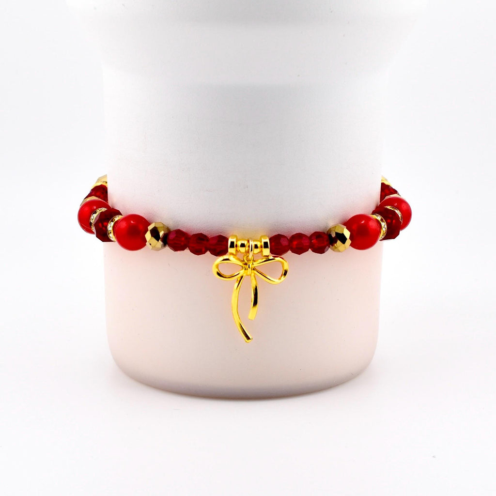 A red beaded bracelet with gold accents and a gold bow charm. The bracelet features large red beads, smaller red beads, and gold-colored spacers. The bow charm hangs from the center of the bracelet.