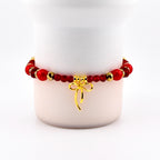A red beaded bracelet with gold accents and a gold bow charm. The bracelet features large red beads, smaller red beads, and gold-colored spacers. The bow charm hangs from the center of the bracelet.