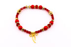 A red beaded bracelet with gold accents and a gold bow charm. The bracelet features red, gold, and clear beads. The bow charm hangs from the center of the bracelet. The bracelet is on a white background.