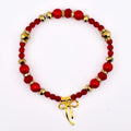 A red beaded bracelet with gold accents and a gold bow charm. The bracelet features a mix of red beads, including round and faceted shapes, interspersed with gold-colored beads and small crystal accents. The gold bow charm hangs at the bottom.