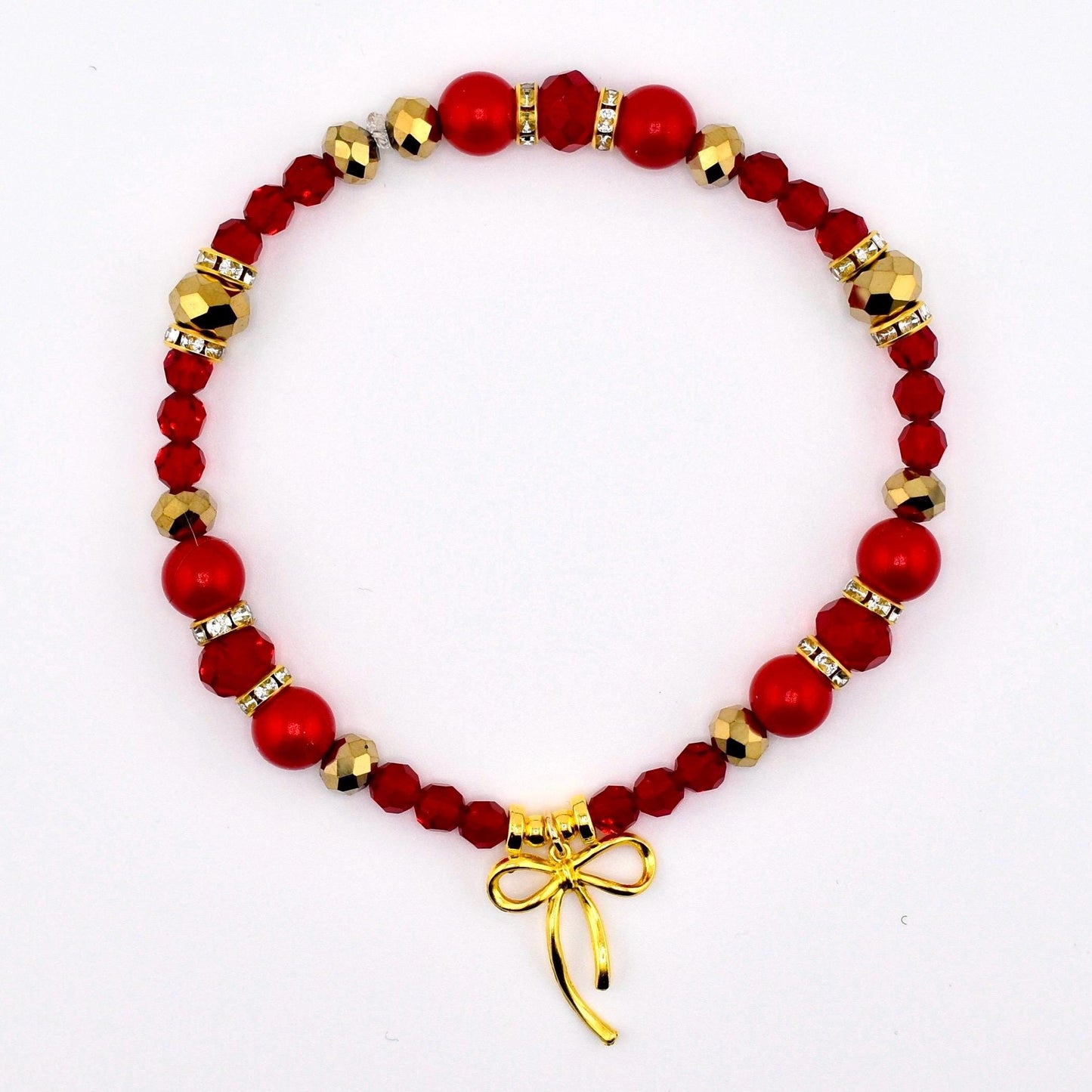 A red beaded bracelet with gold accents and a gold bow charm. The bracelet features a mix of red beads, including round and faceted shapes, interspersed with gold-colored beads and small crystal accents. The gold bow charm hangs at the bottom.