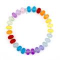 A colorful bracelet featuring a rainbow of glass beads. The beads are oval-shaped and strung together with a silver-colored string. The bracelet showcases a vibrant spectrum of colors, including red, orange, yellow, green, blue, and purple.