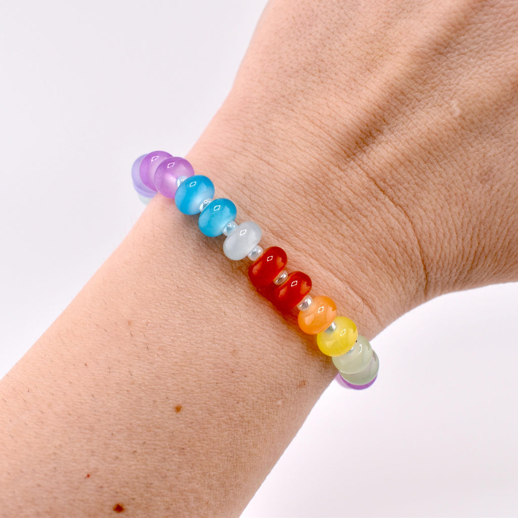 A rainbow-colored beaded bracelet with heart-shaped red beads. The bracelet features beads in shades of purple, blue, white, red, orange, yellow, and green. The bracelet is worn on a wrist.