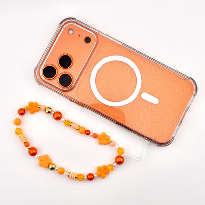 An orange phone with a clear border and a white circular design. A beaded phone strap in shades of orange, yellow, and gold is attached. The strap features flower and bead accents.