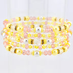 Stack of beaded bracelets in shades of yellow, pink, and white. The bracelets feature a variety of beads, including pearls, crystals, and smaller accent beads. Some sections have gold-colored spacers. The bracelets are stacked together.