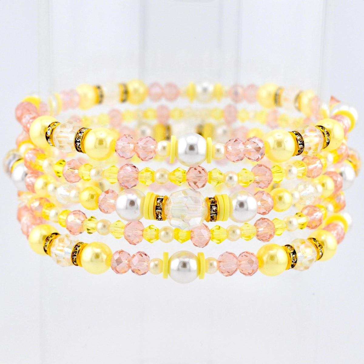 Stack of beaded bracelets in shades of yellow, pink, and white. The bracelets feature a variety of beads, including pearls, crystals, and smaller accent beads. Some sections have gold-colored spacers. The bracelets are stacked together.