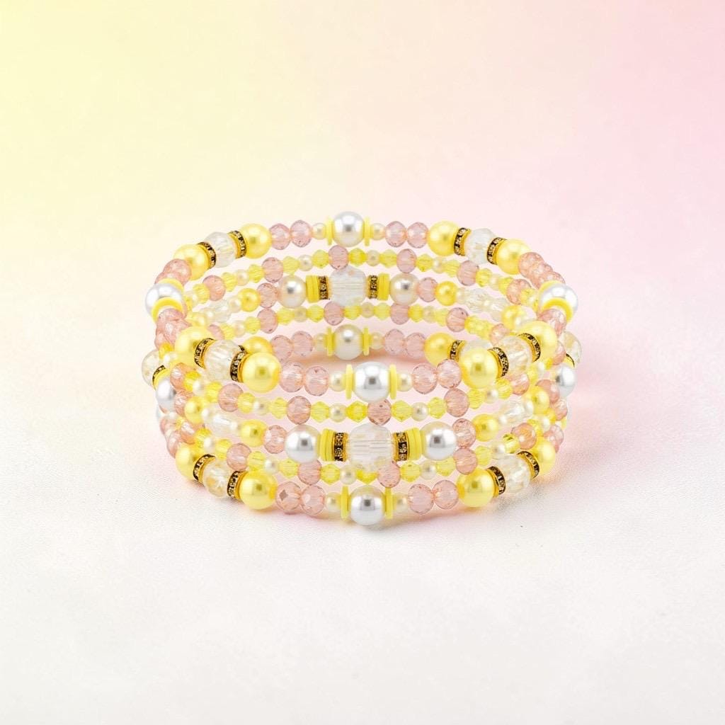 A multi-strand bracelet with yellow, pink, white, and silver beads. The bracelet features a spiral design with a mix of round and faceted beads. The beads are strung together with a flexible wire, creating a layered effect.