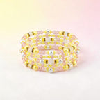 A multi-strand bracelet with yellow, pink, white, and silver beads. The bracelet features a spiral design with a mix of round and faceted beads. The beads are strung together with a flexible wire, creating a layered effect.