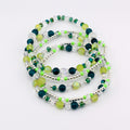 A collection of beaded bracelets in shades of green, teal, and clear. The bracelets feature a mix of round and faceted beads, interspersed with silver-colored spacers. The bracelets are arranged in a layered, circular pattern.
