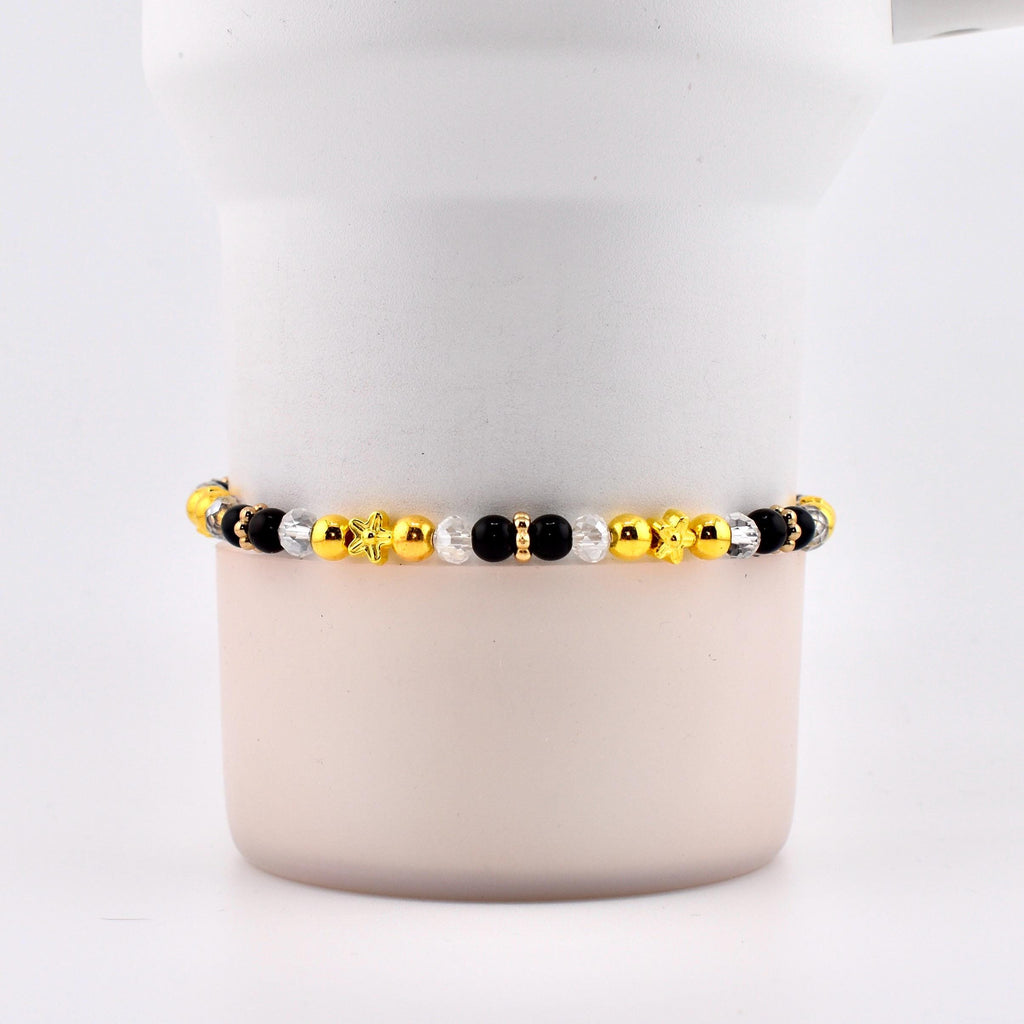 A beaded bracelet featuring a mix of gold, black, and clear beads. The bracelet includes star and flower-shaped accents. The beads are strung together, creating a stylish accessory.
