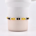 A beaded bracelet featuring a mix of gold, black, and clear beads. The bracelet includes star and flower-shaped accents. The beads are strung together, creating a stylish accessory.