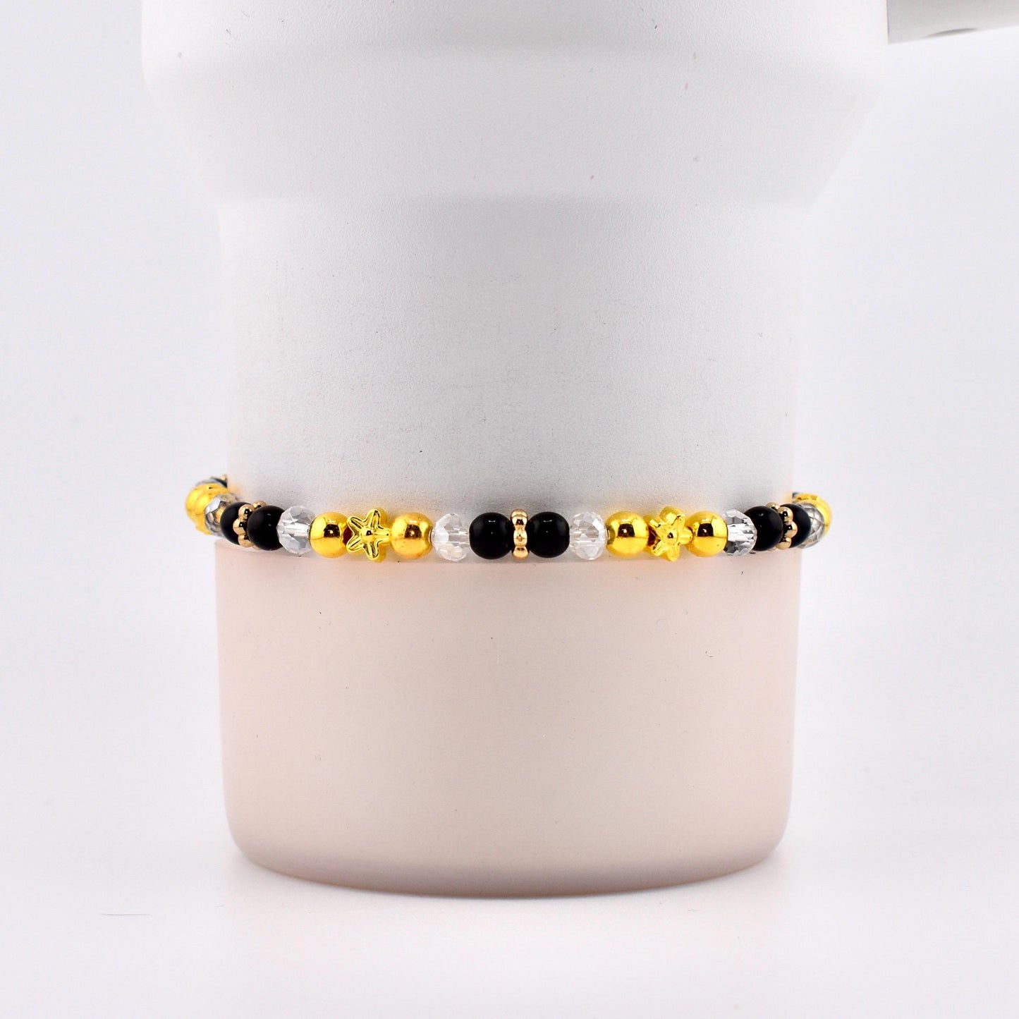 A beaded bracelet featuring a mix of gold, black, and clear beads. The bracelet includes star and flower-shaped accents. The beads are strung together, creating a stylish accessory.