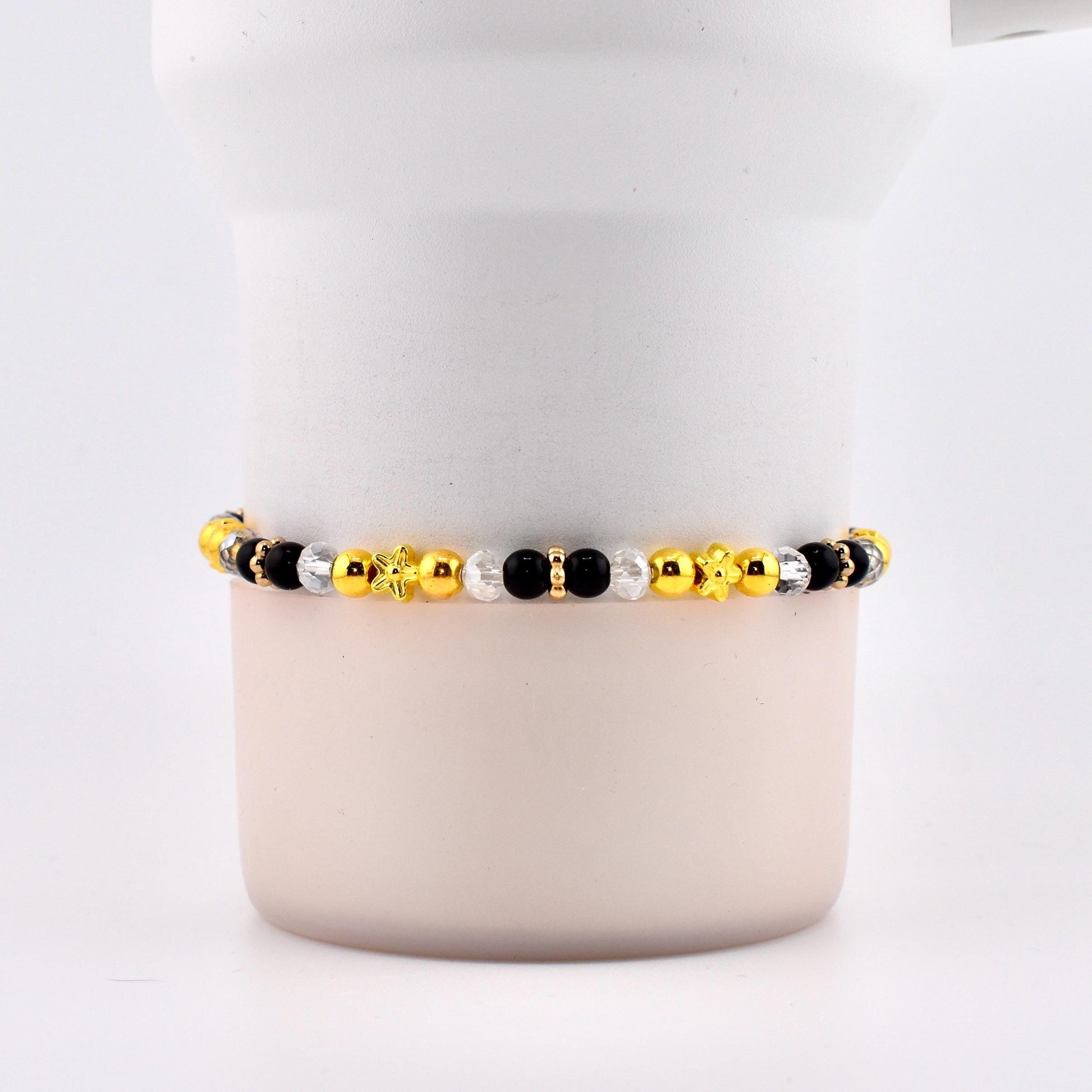 A beaded bracelet featuring a mix of gold, black, and clear beads. The bracelet includes star and flower-shaped accents. The beads are strung together, creating a stylish accessory.