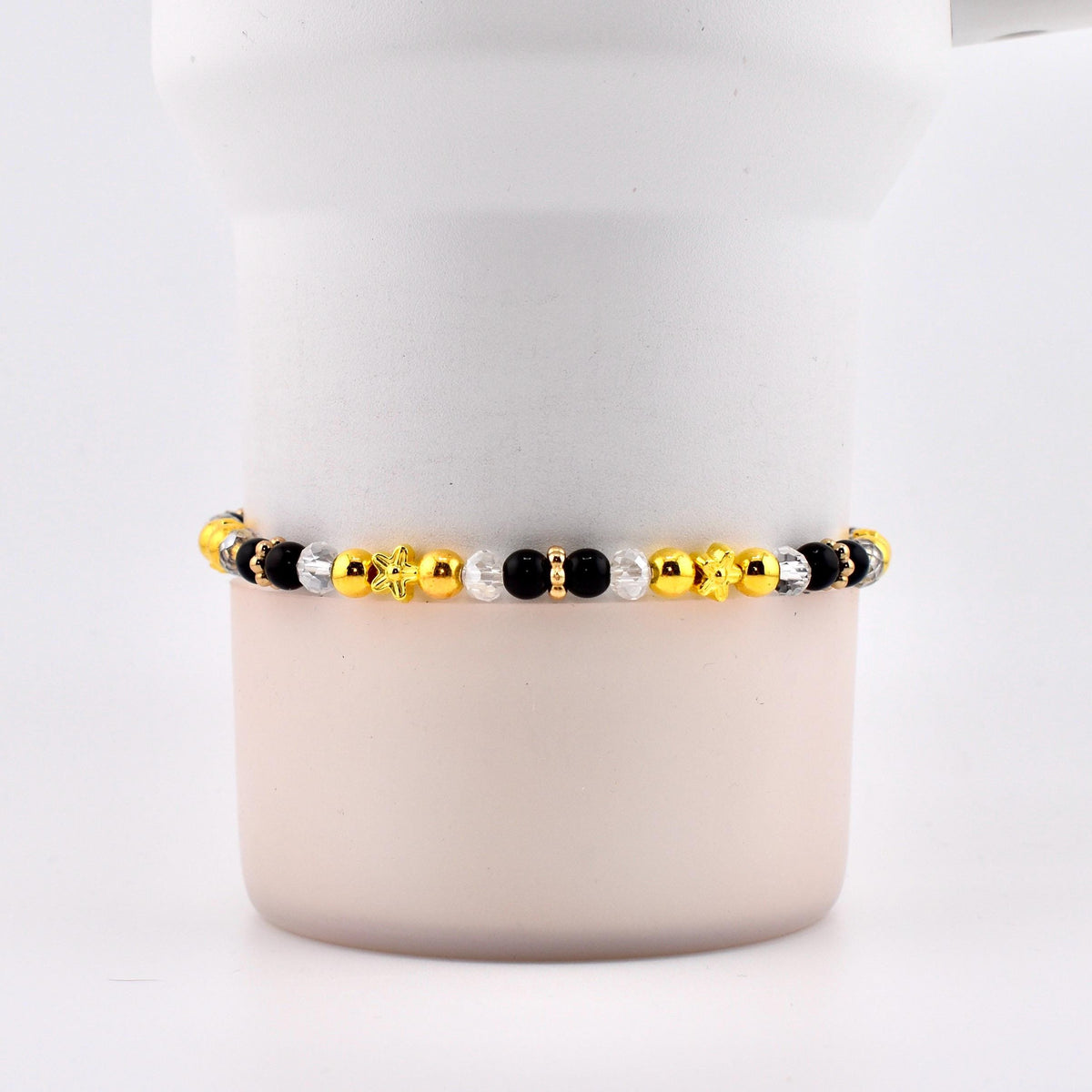 A beaded bracelet featuring a mix of gold, black, and clear beads. The bracelet includes star and flower-shaped accents. The beads are strung together, creating a stylish accessory.
