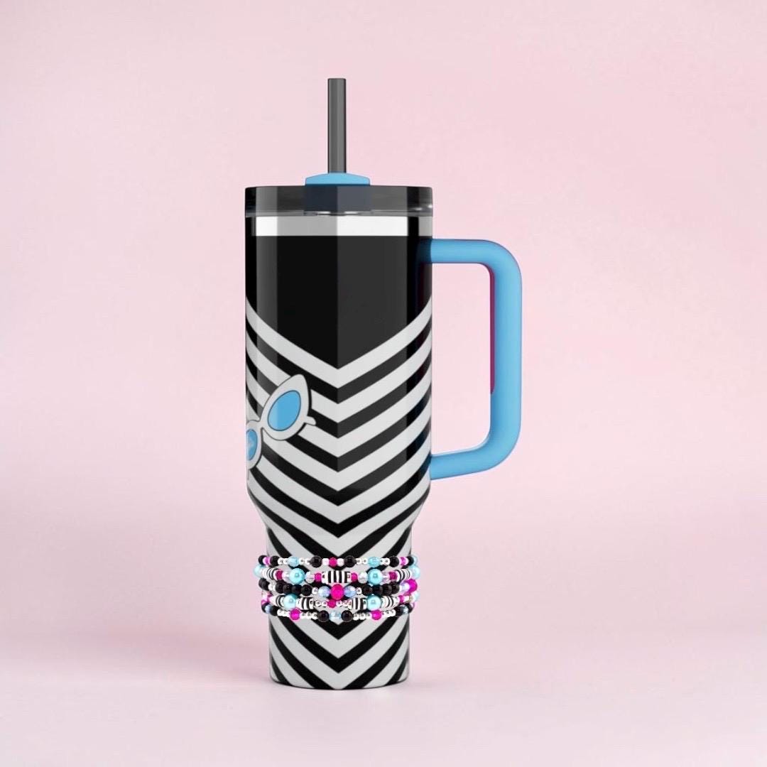 A black and white chevron-patterned tumbler with a blue handle and straw. The tumbler features a sunglasses graphic and is adorned with a beaded bracelet. The design is modern and stylish, perfect for carrying cold beverages.