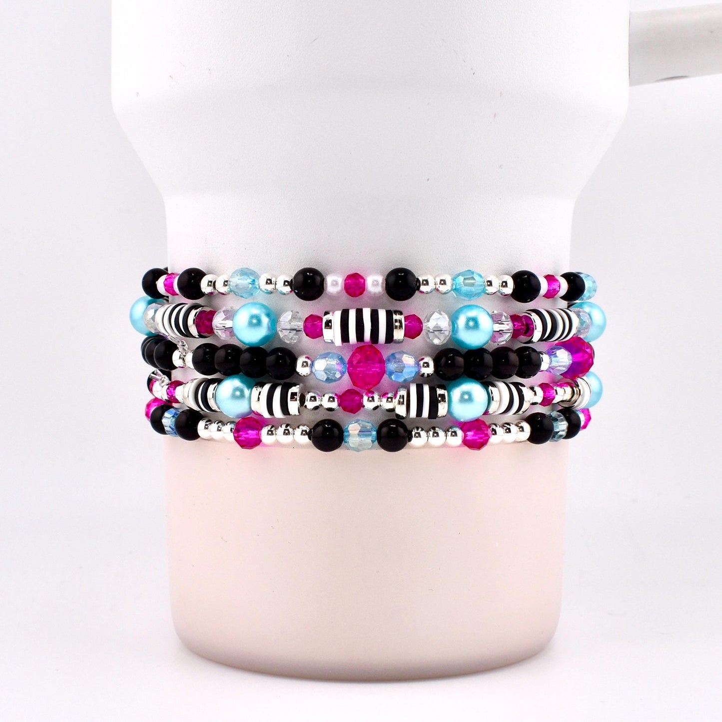 Stack of beaded bracelets in shades of black, pink, blue, and silver. The bracelets feature a variety of beads, including small black and pink beads, larger blue beads, and silver accents. Some bracelets have striped beads.