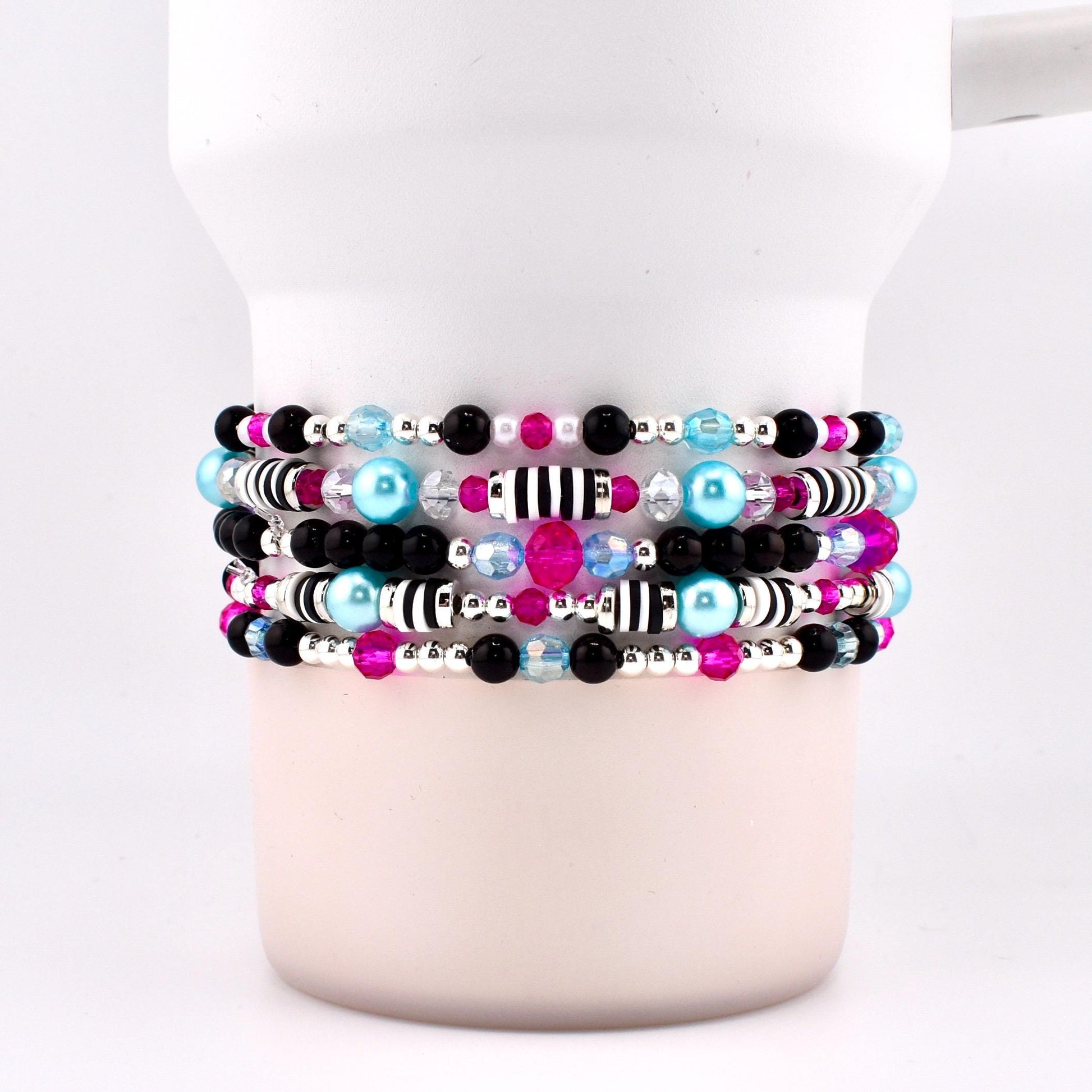 Stack of beaded bracelets in shades of black, pink, blue, and silver. The bracelets feature a variety of beads, including small black and pink beads, larger blue beads, and silver accents. Some bracelets have striped beads.