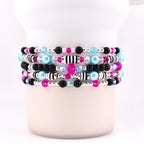 Stack of five beaded bracelets with a variety of beads. The bracelets feature black, silver, pink, light blue, and clear beads. Some bracelets have black and white striped beads.