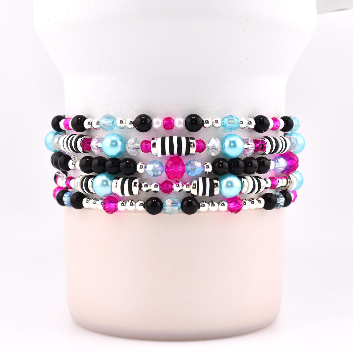 Stack of five beaded bracelets with a variety of beads. The bracelets feature black, silver, pink, light blue, and clear beads. Some bracelets have black and white striped beads.