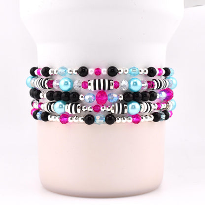 Stack of five beaded bracelets with a variety of beads. The bracelets feature black, silver, pink, light blue, and clear beads. Some bracelets have black and white striped beads.