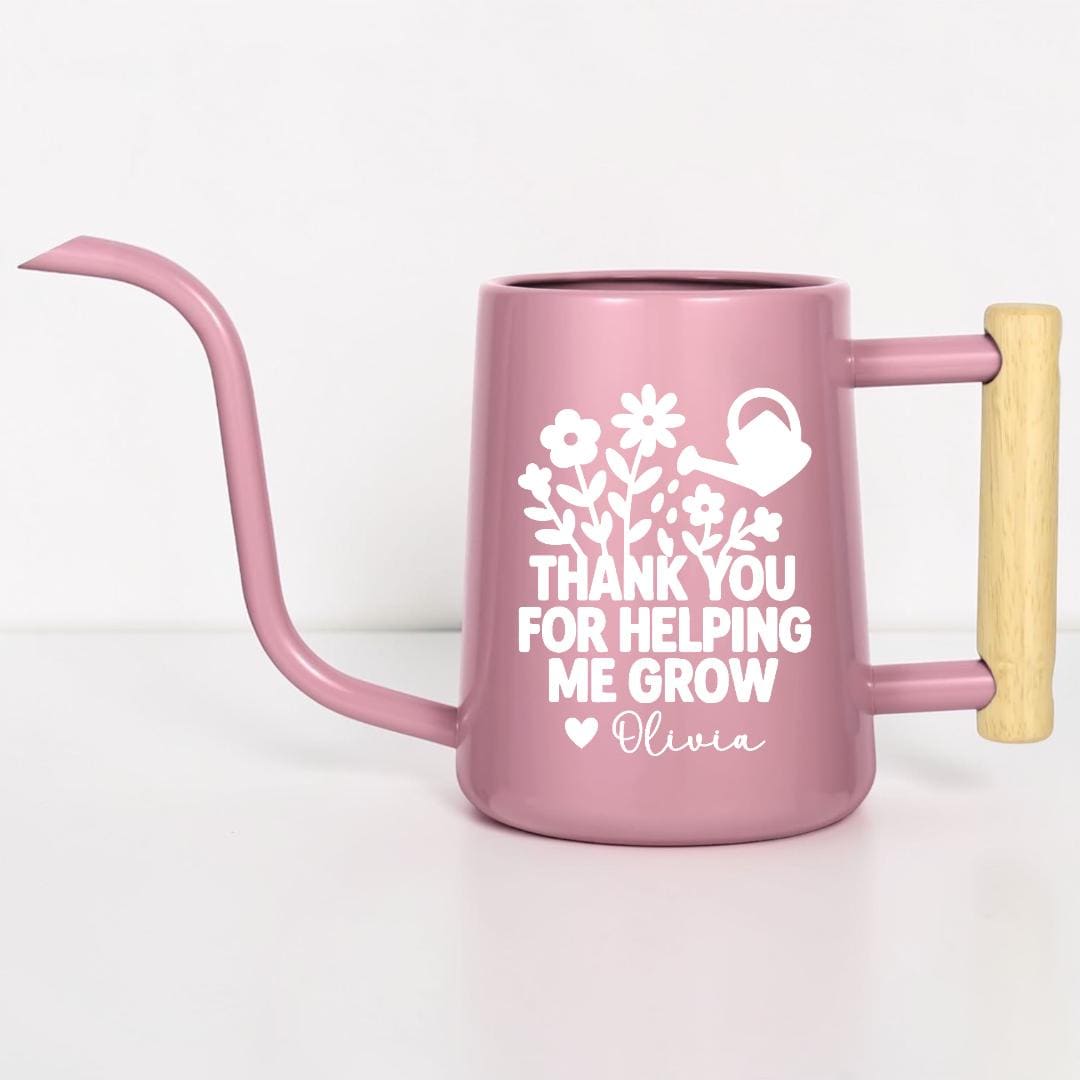A pink watering can with a long spout and wooden handle. The can features white floral and watering can graphics, along with the text "THANK YOU FOR HELPING ME GROW" and a name. Ideal for gardening.