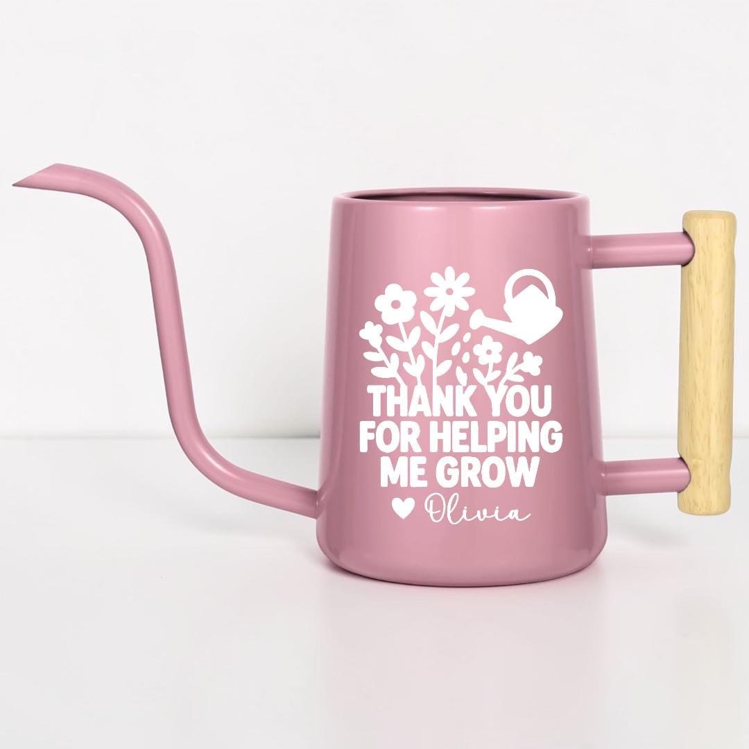 A pink watering can with a long spout and wooden handle. The can features white floral and watering can graphics, along with the text "THANK YOU FOR HELPING ME GROW" and a name. Ideal for gardening.