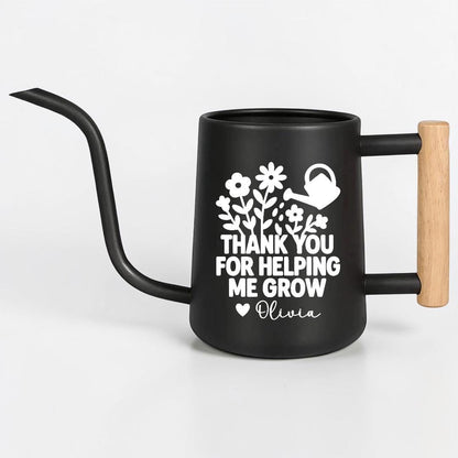 Black watering can with a long, curved spout and a wooden handle. The can features a white floral design and the text "THANK YOU FOR HELPING ME GROW" with the name "Olivia".