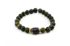 A beaded bracelet featuring olive green round beads and a central dark gray, rectangular bead. Gold-colored spacers flank the central bead. The bracelet is on a white background.