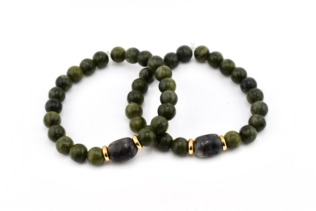 Two beaded bracelets. Each bracelet features olive green round beads and a dark gray, oval-shaped bead with gold-colored accents. The bracelets are displayed on a white background.