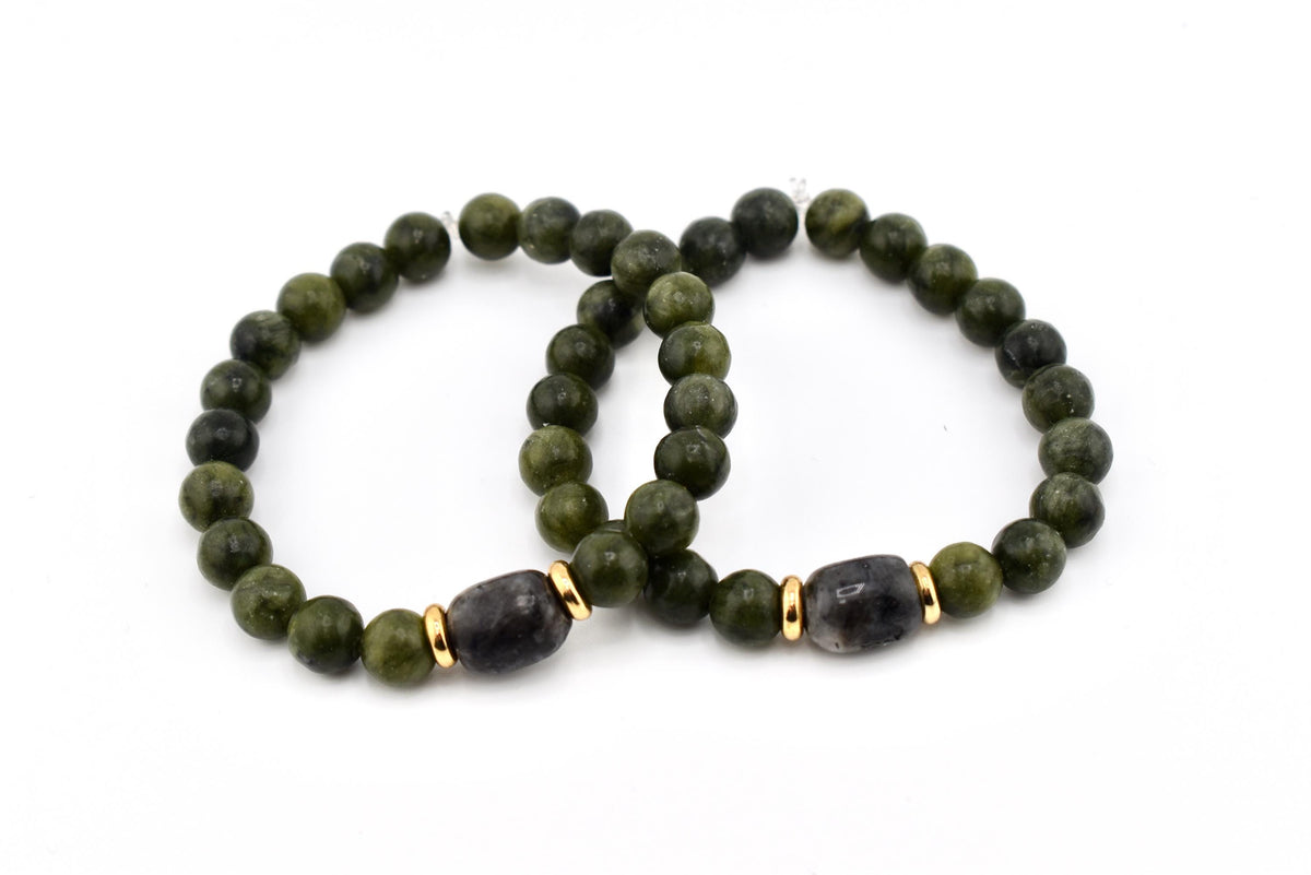 Two beaded bracelets. Each bracelet features olive green round beads and a dark gray, oval-shaped bead with gold-colored accents. The bracelets are displayed on a white background.