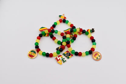 Three beaded bracelets with red, yellow, green, and black beads. Each bracelet has charms with flags, the word "LOVE", and a round charm with text. The bracelets are on a white background.