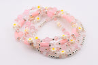 Several beaded bracelets in shades of pink, white, and silver. The bracelets feature a mix of beads, including clear crystal, pink round beads, and small white daisy-shaped beads with yellow centers. The bracelets are layered.