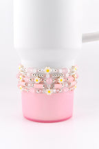 Stack of five beaded bracelets in shades of pink and white, adorned with small daisy accents. The bracelets are wrapped around a white mug with a pink base, creating a cohesive and stylish accessory.