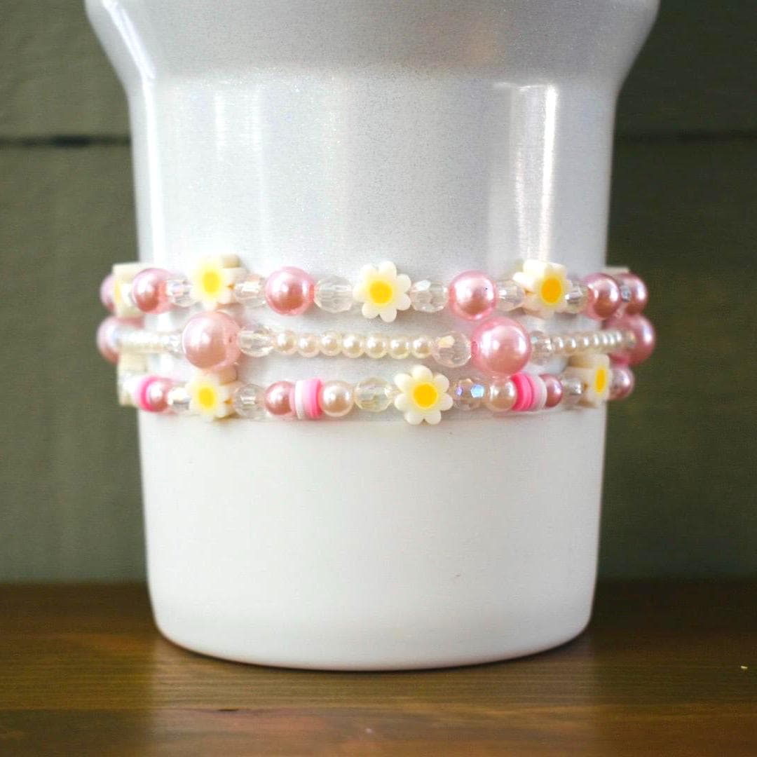 Three beaded bracelets with pink and white beads and yellow flower charms.