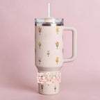 A light pink insulated tumbler with a handle, lid, and straw. The tumbler is decorated with small floral bouquets. A stack of beaded bracelets in shades of pink and white is wrapped around the base of the tumbler.