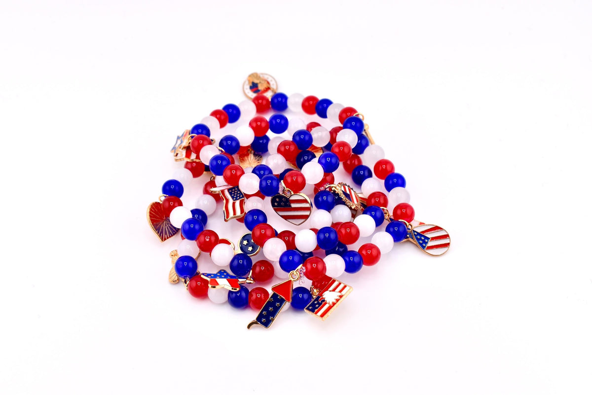 A collection of red, white, and blue beaded bracelets with patriotic charms. Charms include American flags, hearts, and fireworks. The bracelets are on a white background.