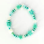 A beaded bracelet featuring a mix of turquoise, white, and clear beads. The bracelet includes star and butterfly-shaped charms. The beads are strung together with a clear elastic cord, creating a playful and whimsical accessory.