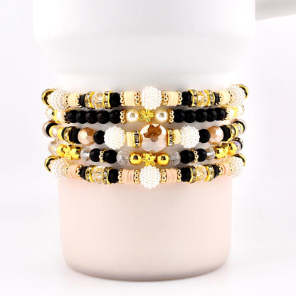 Stack of beaded bracelets in various colors, including gold, black, cream, and peach. The bracelets feature a mix of beads, including round, faceted, and pearl-like beads. Some bracelets have gold accents and star-shaped beads.