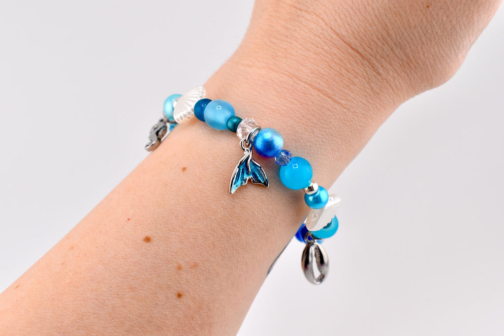 Blue ocean-themed beaded charm bracelet with mermaid tail charm, silver cowrie shell charms, white seashell beads and mixed blue pearl and crystal beads – handmade beach jewelry coastal boho bracelet