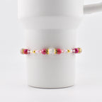 A beaded bracelet with pink, gold, and clear beads. The bracelet features a central cluster of larger beads, including a clear, faceted bead and several pink beads. The bracelet is strung on a thin, flexible cord.