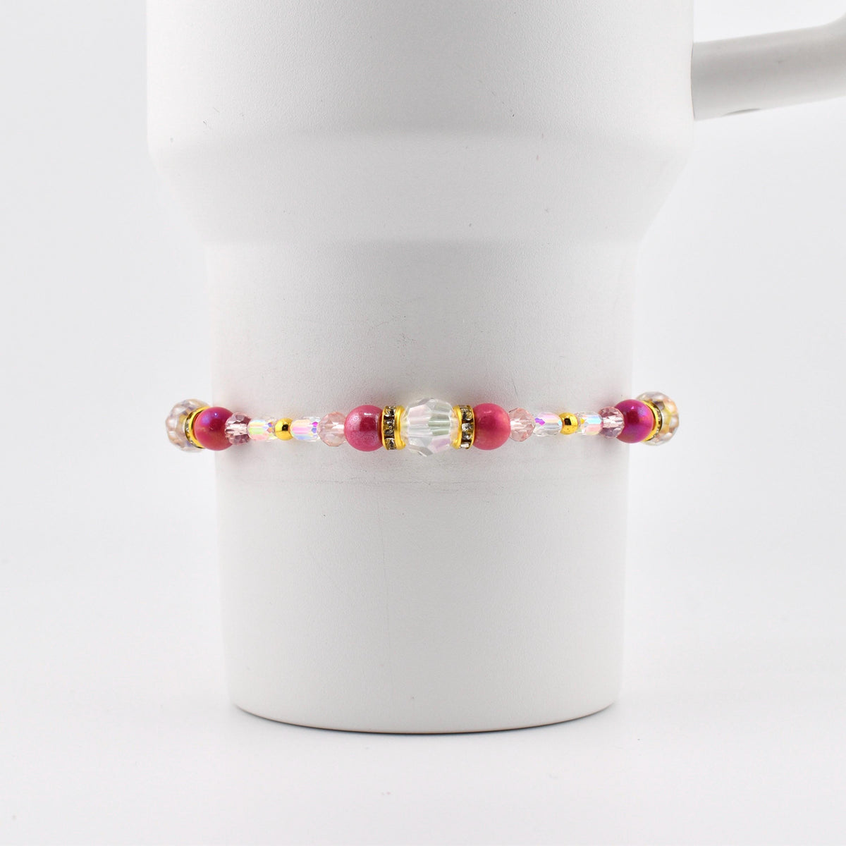 A beaded bracelet with pink, gold, and clear beads. The bracelet features a central cluster of larger beads, including a clear, faceted bead and several pink beads. The bracelet is strung on a thin, flexible cord.