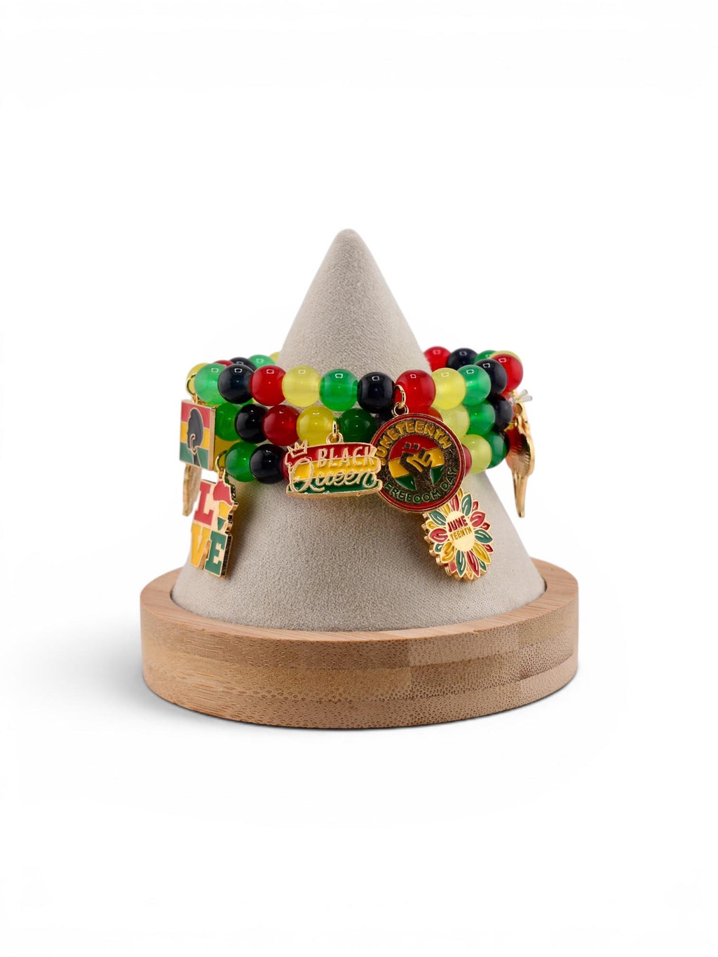 A display of beaded bracelets in red, yellow, green, and black. Each bracelet has charms with text and images, including "Black Queen" and "June Teenth". The bracelets are displayed on a wooden and felt stand.