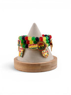 A display of beaded bracelets in red, yellow, green, and black. Each bracelet has charms with text and images, including "Black Queen" and "June Teenth". The bracelets are displayed on a wooden and felt stand.