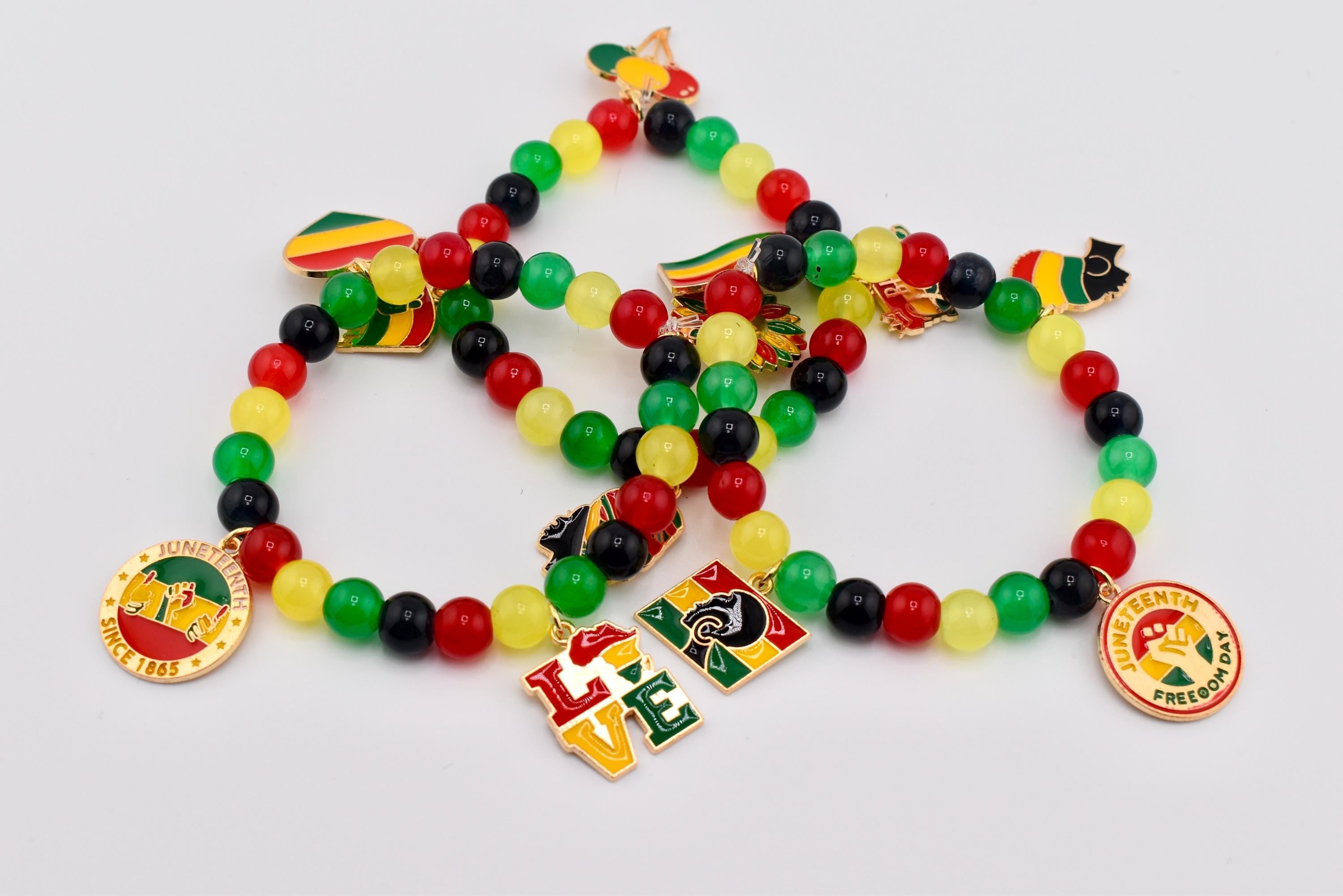 Beaded bracelets in red, yellow, green, and black. Each bracelet features Juneteenth-themed charms and pendants with the word "LOVE" and the phrase "Juneteenth Freedom Day" on them. The bracelets are on a white background.
